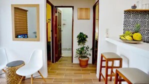 Un couloir avec une plante en pot, une porte en bois et un mur blanc orné d’une étagère décorative.