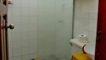 A bathroom with a shower, toilet, and a sink. There are shelves with towels and a potted plant.