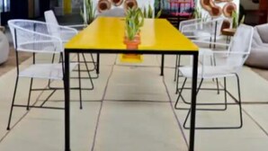 Un comedor con una mesa amarilla, sillas blancas y una pared decorada con diseños circulares de madera.