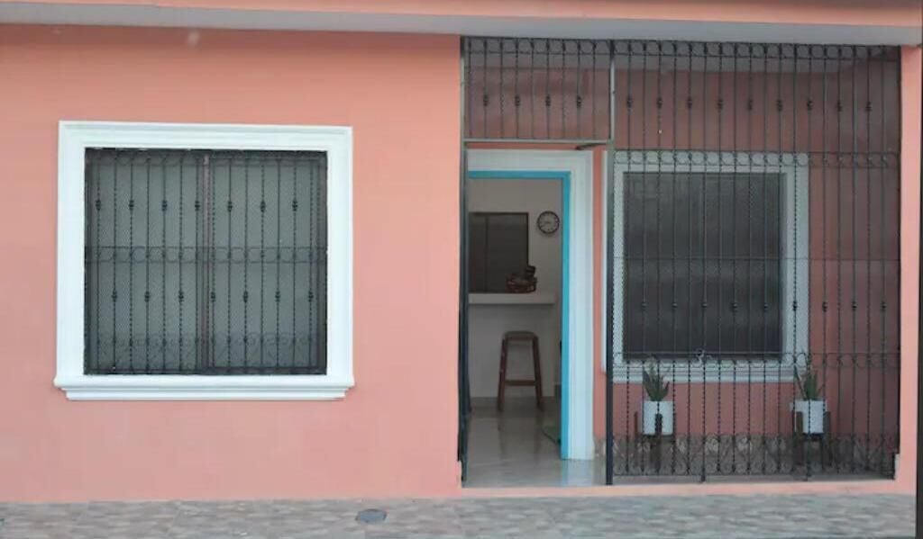 Ein Gebäude mit rosa Fassade, einem Fenster mit Metallgitter und einer Tür zu einem Innenraum.