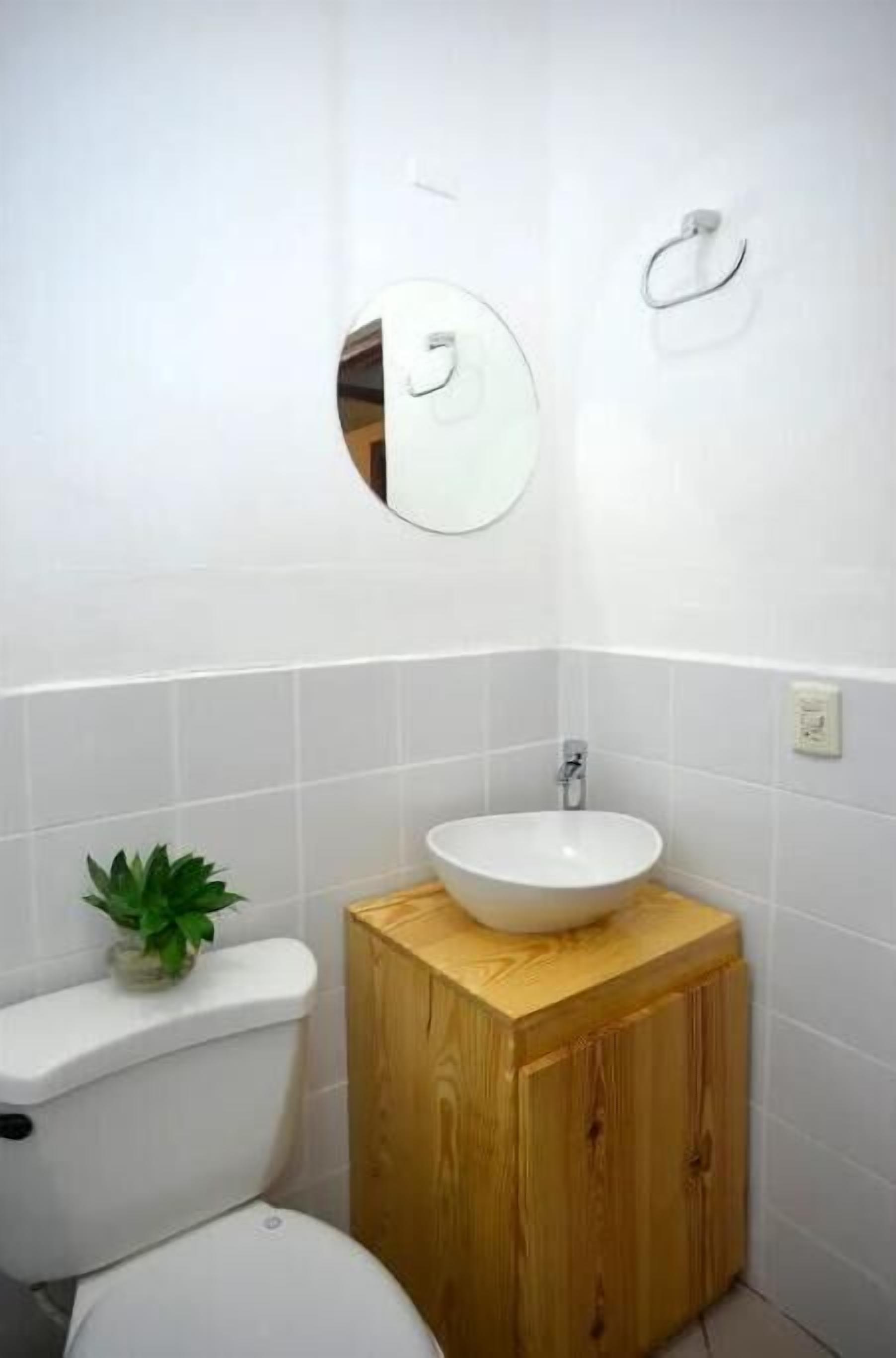 A bathroom with a white toilet, a wooden cabinet with a sink, and a mirror on the wall.