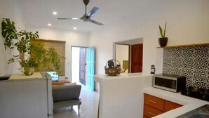 Una cocina moderna con encimeras blancas, un microondas y un fregadero. Hay un ventilador de techo y una planta en maceta sobre la encimera.
