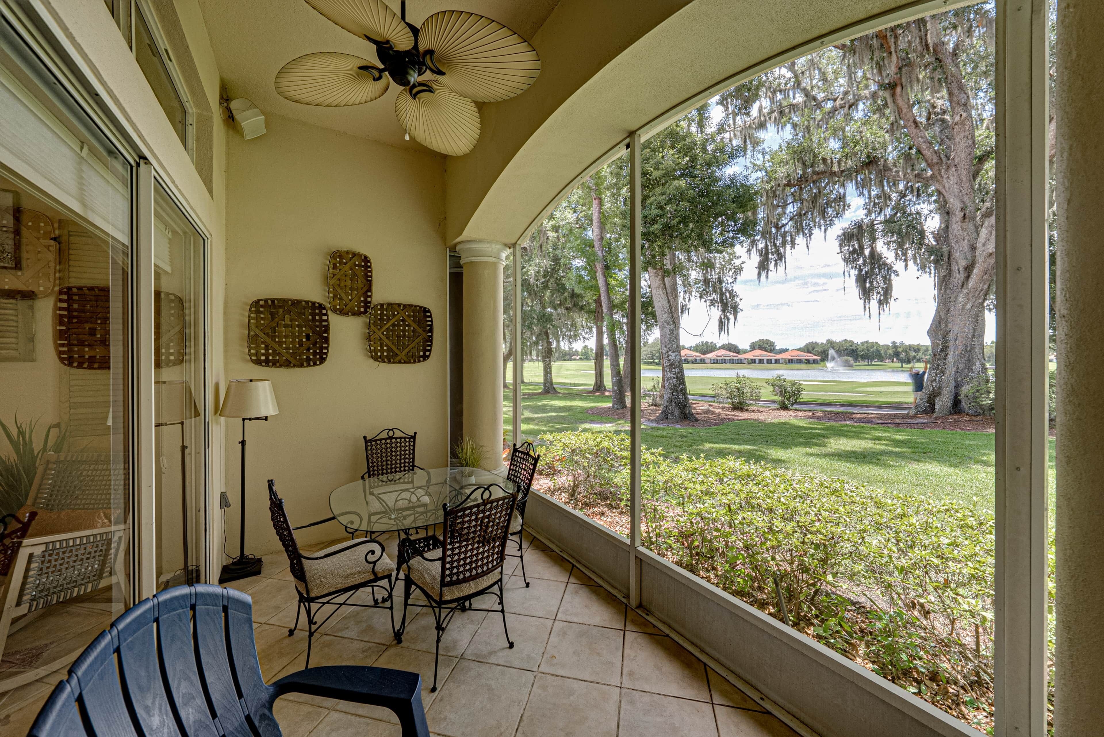 Un patio techado con mesa y sillas, un ventilador de techo y vista a un campo de golf.