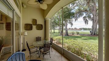 Un patio techado con mesa y sillas, un ventilador de techo y vista a un campo de golf.