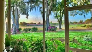 A view from a window overlooking a lush garden with trees and a grassy field.