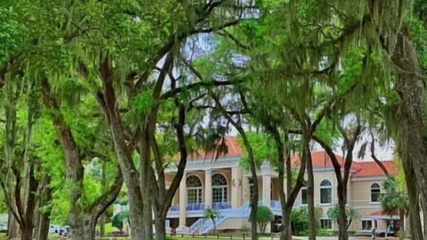 A large building with a classical architectural style, surrounded by mature trees and well-maintained lawns.