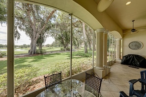 A covered patio with a glass table and chairs, overlooking a well-manicured lawn and trees.