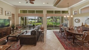 A spacious living room with a large TV, leather sofa, dining area, and a ceiling fan.