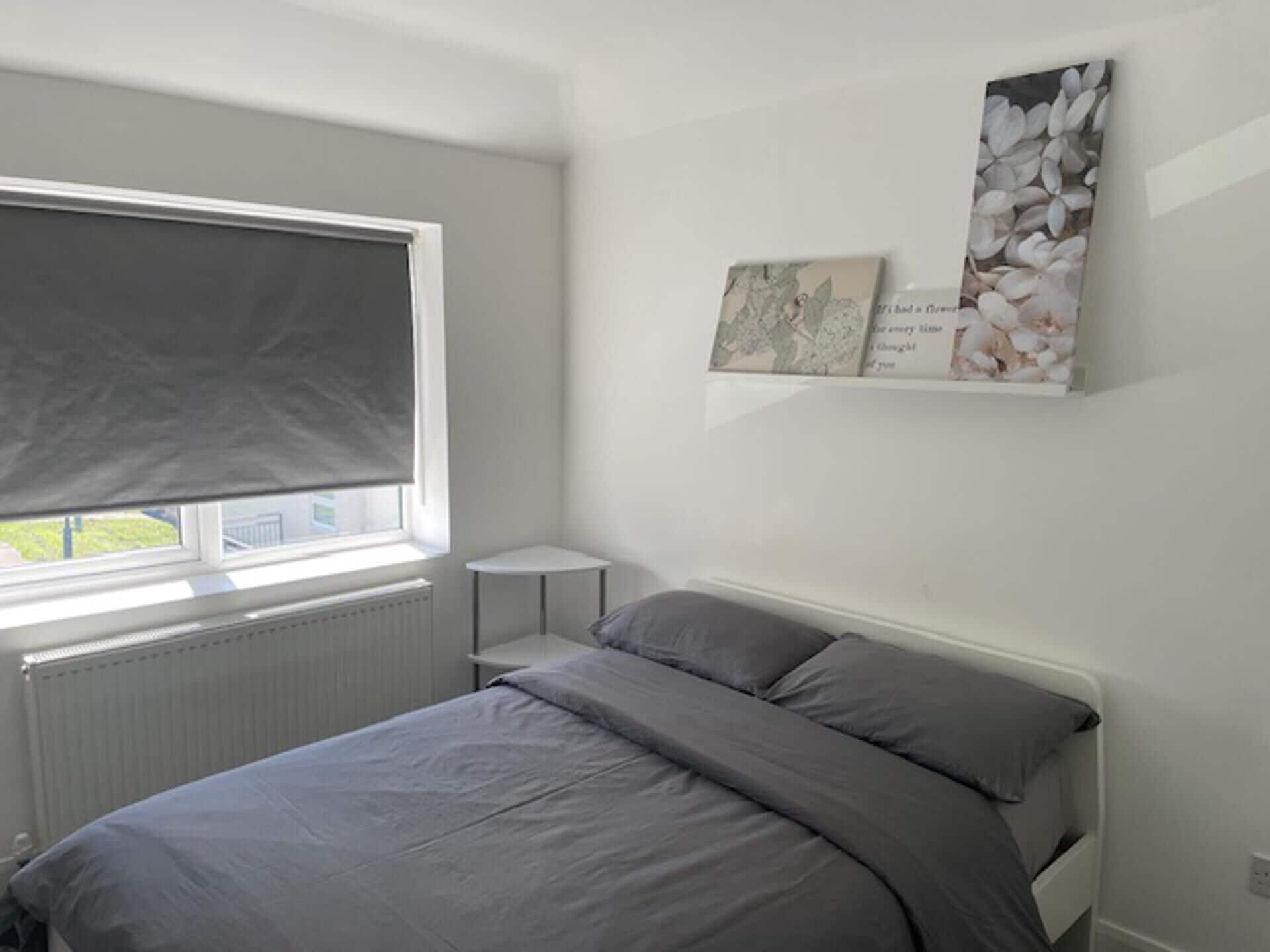 A bedroom with a bed, a window with a blind, a radiator, and two wall-mounted picture frames.