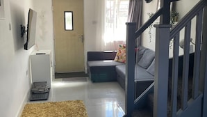 A modern living room with a grey sofa, a small rug, a staircase, and a door leading to another room. - 1bedhouse- London-sleeps 4- Close to Attractions (London)