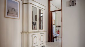 A white, ornate cabinet with glass doors, a framed picture on the wall, and a door leading to another room.