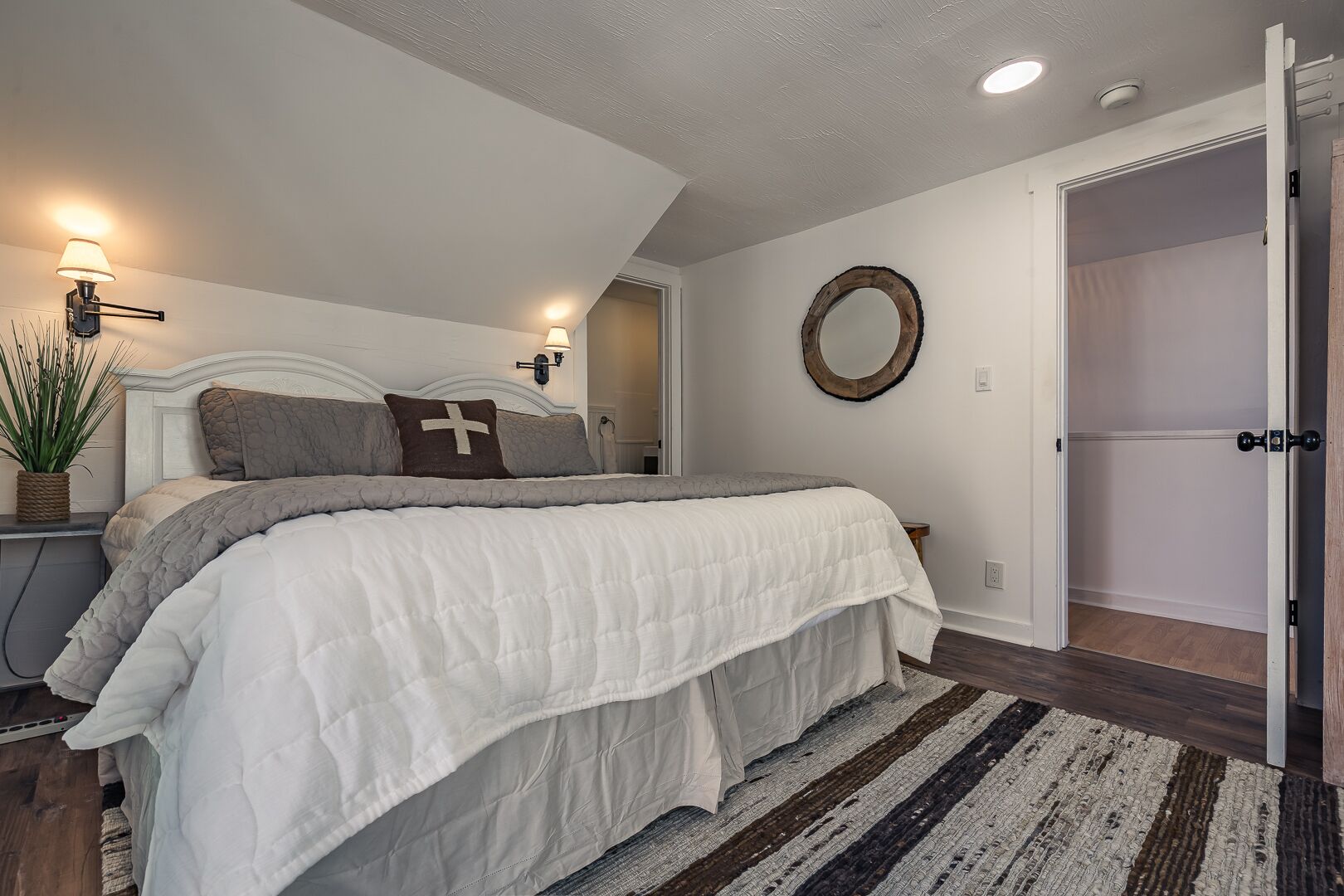 Une chambre à coucher avec un grand lit, des lampes de chevet, un miroir et une porte donnant sur une autre pièce.