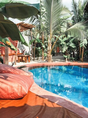 Una piscina rodeada de plantas tropicales y mobiliario de madera.