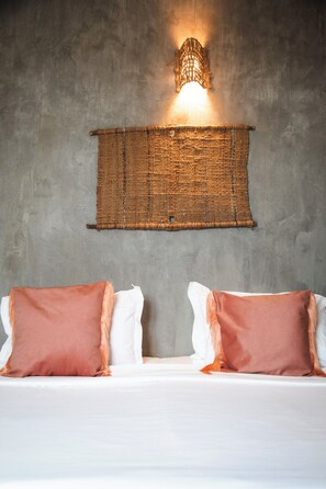 Un lit avec deux oreillers, une tapisserie murale tissée et un luminaire fixé au mur.