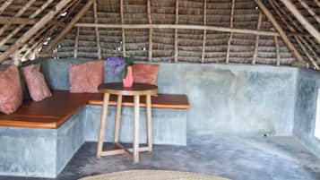 Um quarto com telhado de colmo, área de estar com almofadas, uma pequena mesa e um tapete de palha.