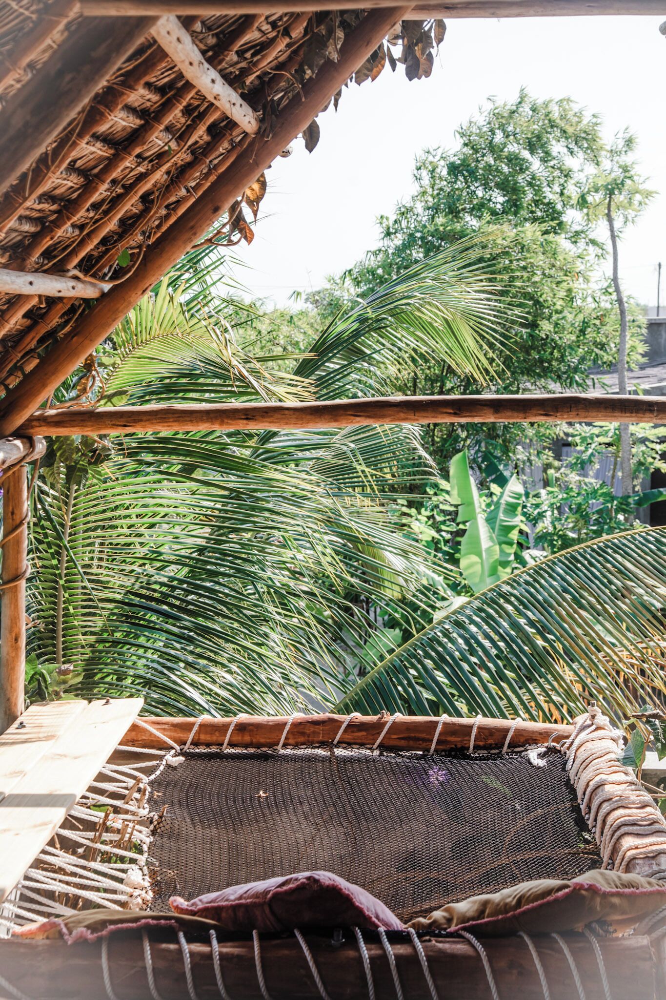 A hammock under a bamboo structure with a view of palm trees.