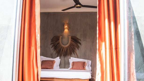 A room with a bed, curtains, a ceiling fan, and a wall-mounted light fixture. - Green Ocean Zanzibar Boutique Hotel (Jambiani)