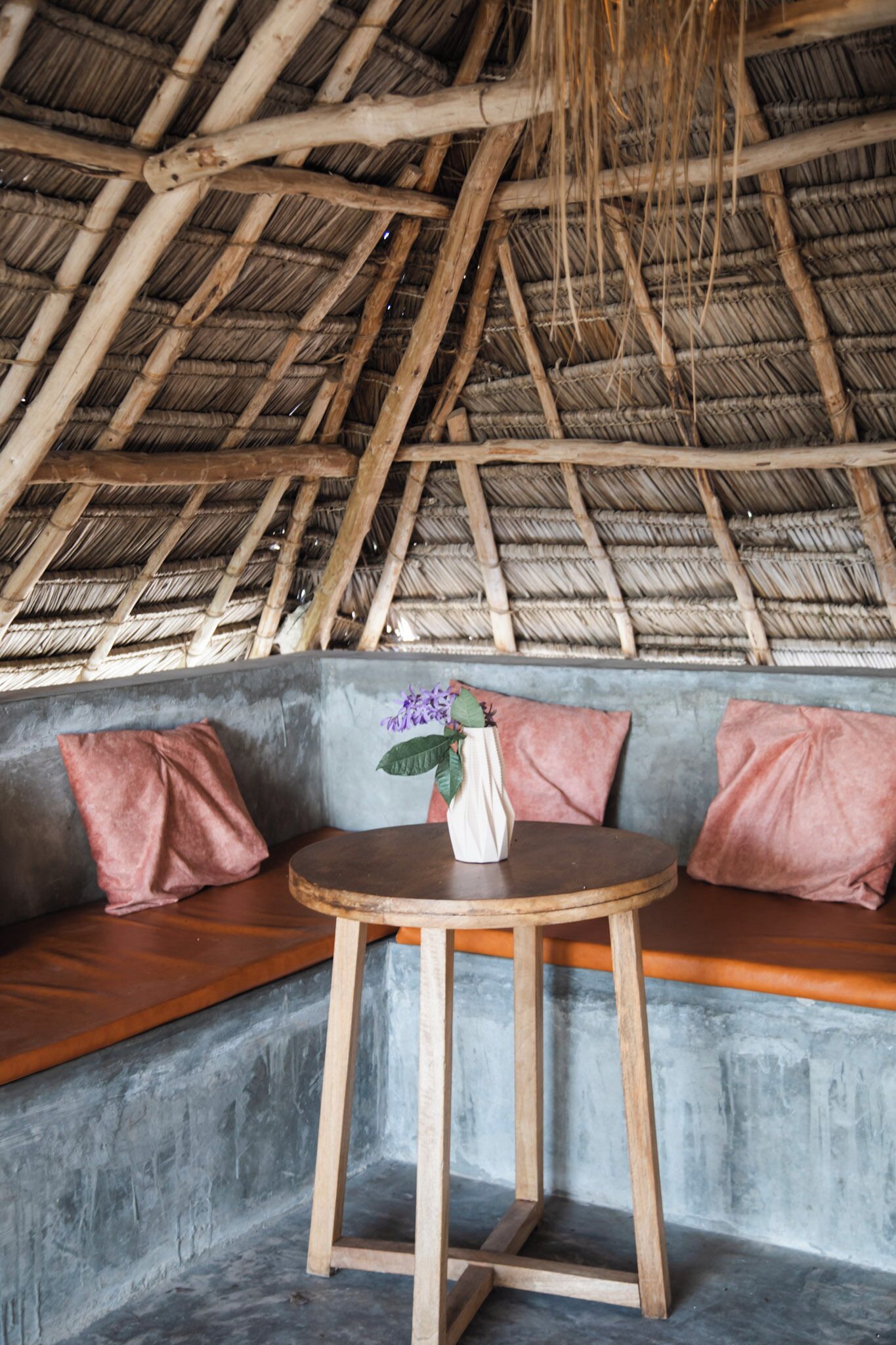 A thatched roof structure, a round wooden table, and a seating area with cushions.