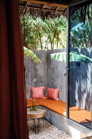 A room with a concrete wall, a bench with cushions, a small round table, and a bottle. - Green Ocean Zanzibar Boutique Hotel (Jambiani)