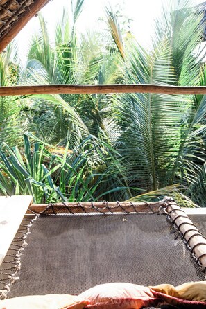 Una hamaca con base de mosquitero, estructura de madera y vista a follaje verde denso.