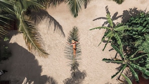 A person lying on a sandy surface surrounded by palm trees. - Green Ocean Zanzibar Boutique Hotel (Jambiani)