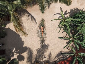 A person lying on a sandy surface surrounded by palm trees. - Green Ocean Zanzibar Boutique Hotel (Jambiani)