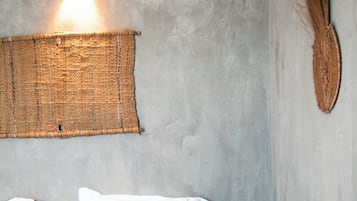 Uma cama com almofadas brancas e cor-de-rosa, um painel de parede tecido e uma luminária fixada na parede.