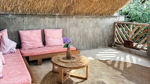 A room with a thatched ceiling, a pink sofa, a round wooden table, and a woven rug. - Green Ocean Zanzibar Boutique Hotel (Jambiani)