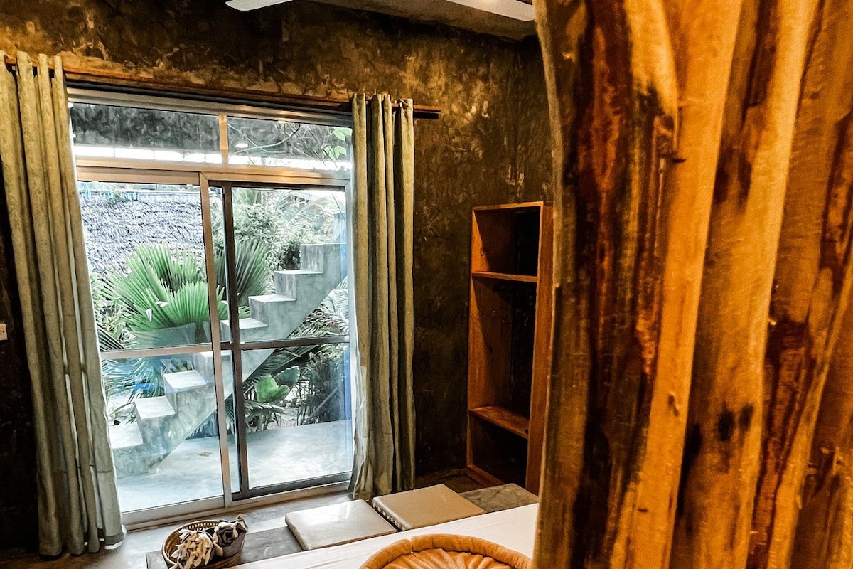 Un dormitorio con cama, ventilador de techo, ventana con cortinas y vistas al exterior.