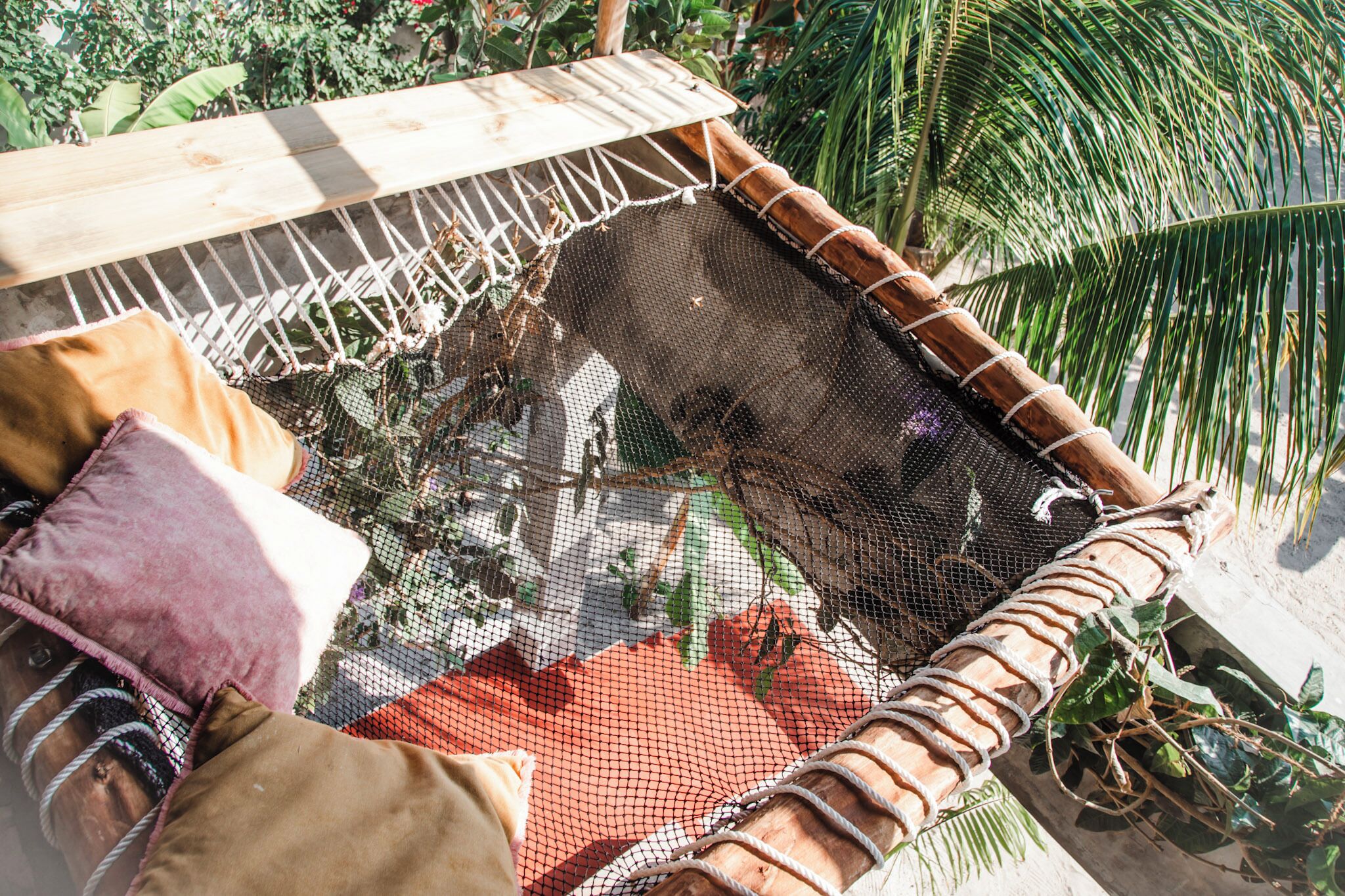 Un hamac doté d’un fond en filet, entouré de verdure et adossé à une structure en bois.