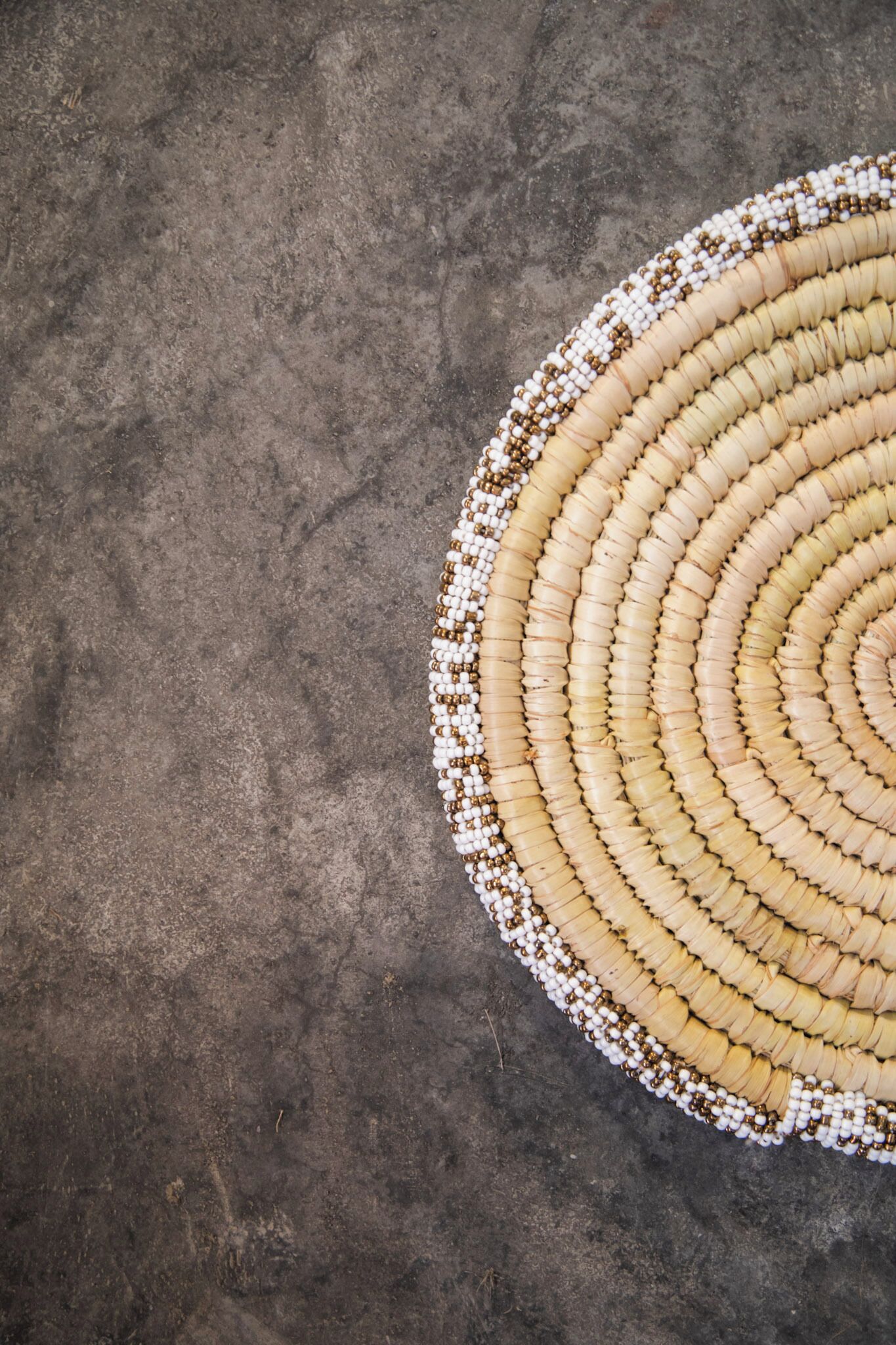 Un tapete circular tejido con un diseño concéntrico, sobre una superficie de concreto texturizado.