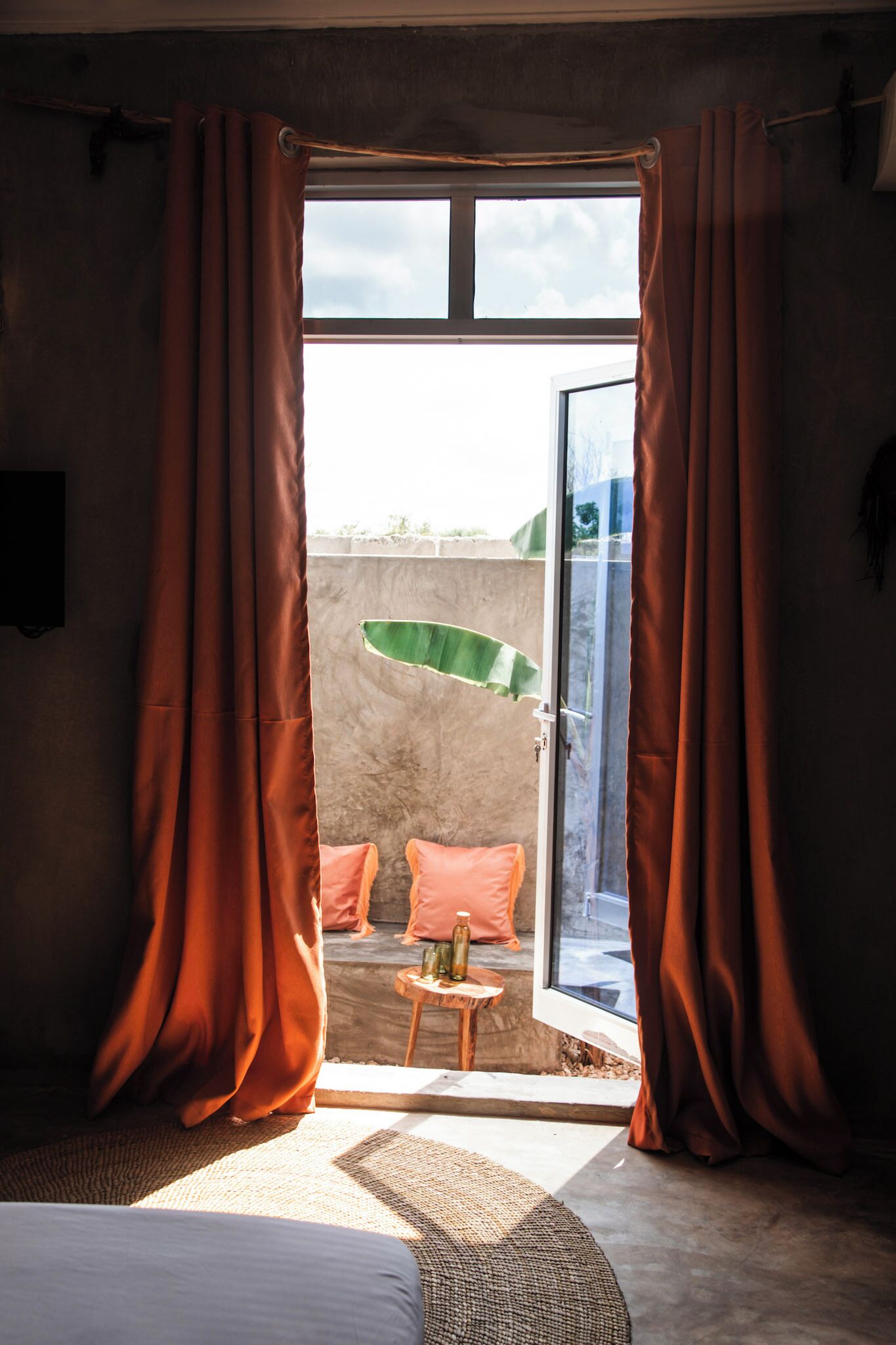 Una habitación con cama, una mesita con botellas y vista a un paraguas verde en el exterior.