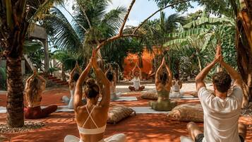 Eine Gruppe übt Yoga im Freien, im Hintergrund Bäume und ein klarer Himmel.