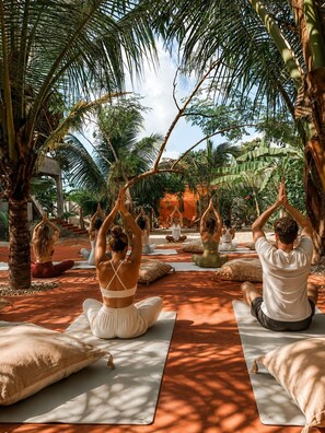 Eine Gruppe übt Yoga im Freien, im Hintergrund Bäume und ein klarer Himmel.