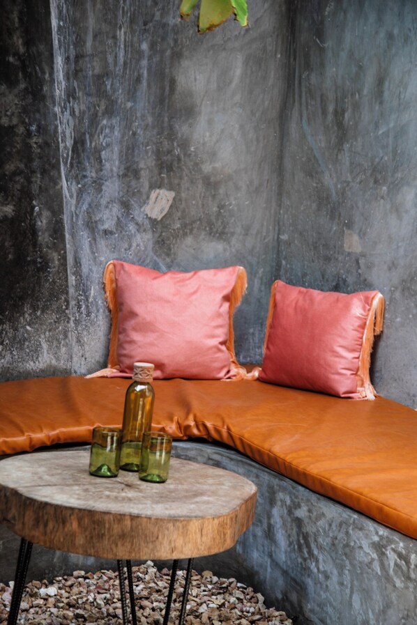 A cozy seating area with a cushioned bench, two pillows, and a small round table with glasses and a bottle.