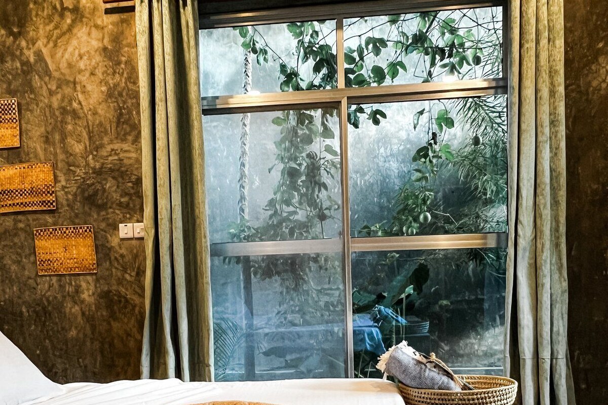 Un dormitorio con un ventanal grande, una cama con cabecera decorativa y una mesita de noche con una cesta de mimbre.