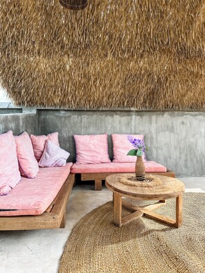 Una habitación con techo tejido, un conjunto de sofá con cojines rosa, una mesa de centro de madera y una alfombra tejida.