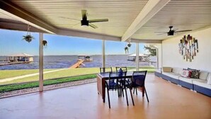 A covered outdoor area with a dining table and chairs, a sofa, and a view of the sea. - Tranquil Lakefront Retreat (Lake Placid)