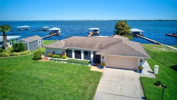 A house with a garage, a lawn, and a dock extending into a body of water. - Tranquil Lakefront Retreat (Lake Placid)