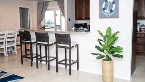 A modern kitchen with a bar area, white chairs, and a large potted plant. - Tranquil Lakefront Retreat (Lake Placid)