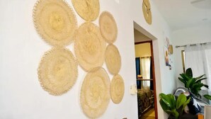 A room with a white wall decorated with circular woven wall hangings. There is a doorway leading to another room with a patterned sofa.