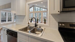 A modern kitchen with a double sink, stainless steel appliances, and a window with a view of trees.