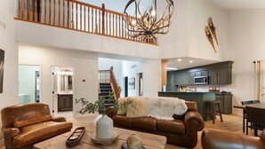 A spacious living room with a high ceiling, a wooden coffee table, leather sofas, and a staircase leading to an upper level. - Lakeside Getaway Theatre, Indoor Pool and Game Room (Gouldsboro)