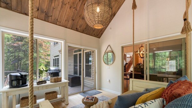A cozy living room with a large window, a swing, and a ceiling light. - Lakeside Getaway Theatre, Indoor Pool and Game Room (Gouldsboro)