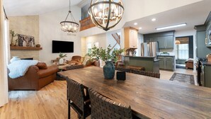 A spacious living area with a wooden dining table, comfortable seating, and a large chandelier. - Lakeside Getaway Theatre, Indoor Pool and Game Room (Gouldsboro)
