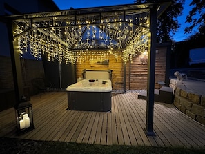 A hot tub under a string-lit pergola on a wooden deck.