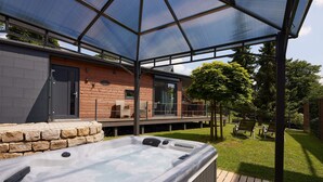 A hot tub under a glass canopy, a wooden deck, and a stone wall. - Gemütliches 4 Ferienhaus mit Whirlpool, Fitness, Infrarotsauna, Ebike, Alpakas (Braunfels)