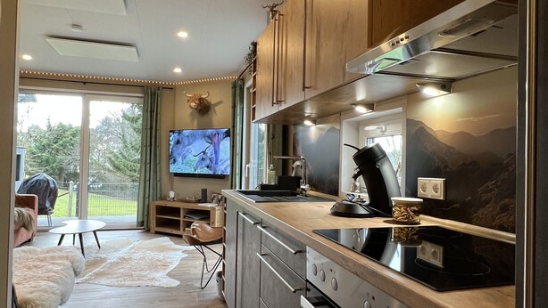 A modern kitchen with stainless steel appliances, wooden cabinets, and a large window overlooking a garden. - Gemütliches 4 Ferienhaus mit Whirlpool, Fitness, Infrarotsauna, Ebike, Alpakas (Braunfels)