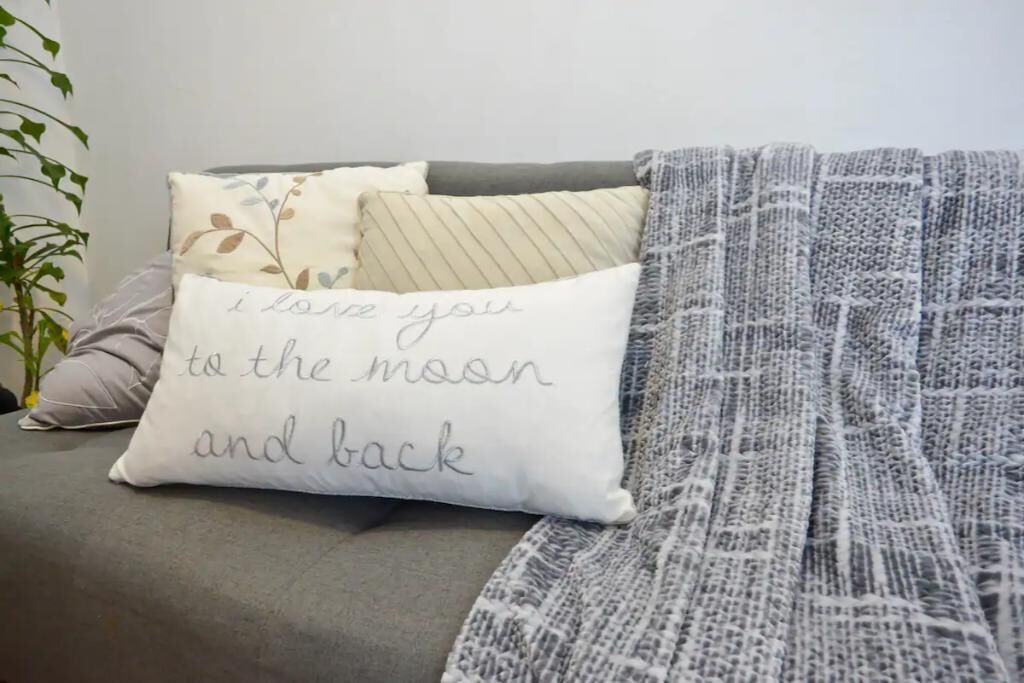 A grey sofa with a white pillow that reads "I love you to the moon and back."