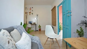 A living room with a sofa, a white chair, a wooden table, and a blue door.
